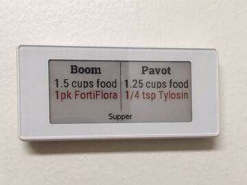 A small display mounted on a wall, showing food and medication for Boom and Pavot.